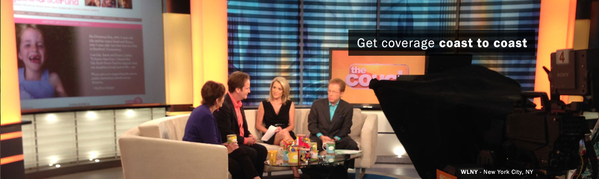 A television studio setting features four co-hosts seated on a couch, discussing while a camera captures the scene. A colorful promotional graphic is displayed behind them.