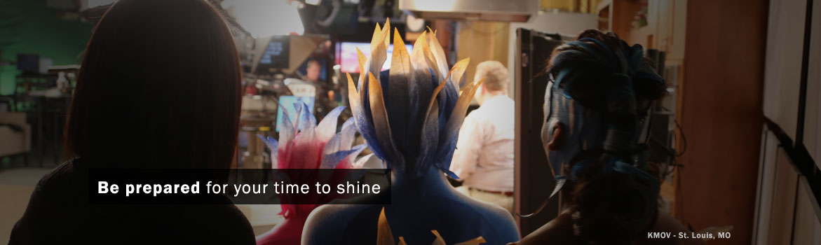 Two individuals with elaborate, colorful hairstyles prepare to appear on camera in a studio setting. The message encourages readiness for performance.